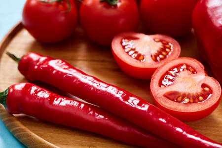 Composition of tomato bunch and halves and sweet pepper on wooden plate, top view, close-up, selective focus.の写真素材