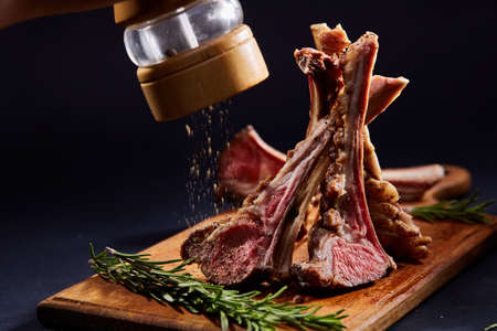 Rack of lamb with rosemary on wooden cutting board over dark background, side view, selective focusの写真素材