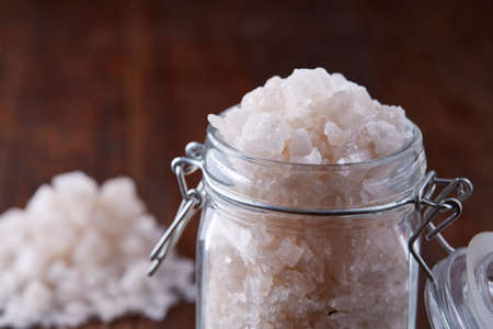 Spa concept. Bath salt pouring out of glass jar on wooden table, close-up, selective focus, shallow...