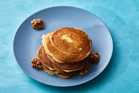 Pile of homemade pancakes with walnuts on blueish plate over blue background, selective focusの写真素材