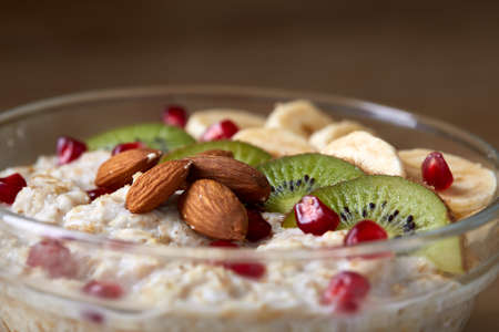 Delicious oatmeal porrige with fruits in glass bowl over rustic wooden background, shallow depth of...