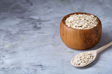 Oat flakes in bowl and wooden spoon isolated on wooden background, close-up, top view, selective focus.の写真素材
