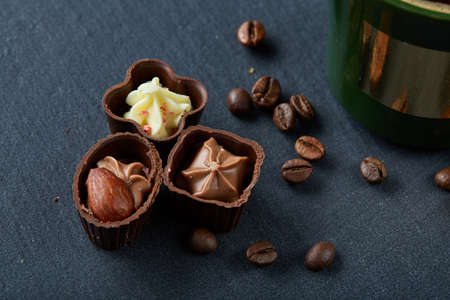 Coffee cup, coffee beans, chocolate candies on stone board over wooden background, selective focus,...