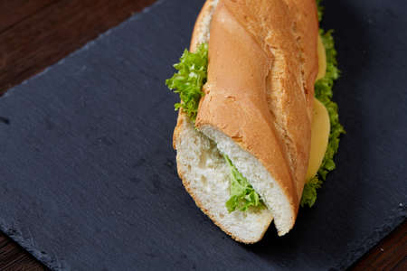 Fresh and tasty sandwich with cheese and vegetables on cutting board over white textured background,...