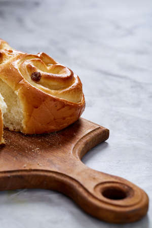 Homemade rose buns with raisins on wooden cutting board over white textured background, close-up, shallow depth of field. Aromatic delicious pastry. Traditional sweet dessert. Food concept.の写真素材