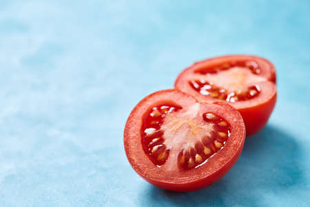 Two halves of tomato placed on blue background, top view, close-up, shallow depth of field, selective focus. Delicious healthy appetizer. Fresh gourmet ingredient. Spring food background. Dietary product. Healthy food concept.の写真素材
