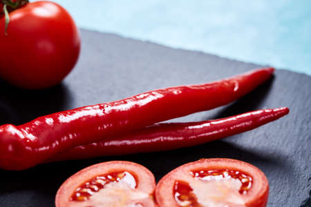 Spring composition of tomato bunch and hot pepper on black flat piece of board over white textured background, top view, close-up. Perfect vegetable still life. Delicious healthy appetizer. Fresh gourmet ingredient. Healthy food concept.の写真素材