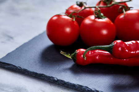 Spring composition of tomato bunch and hot pepper on black flat piece of board over white textured background, top view, close-up. Perfect vegetable still life. Delicious healthy appetizer. Fresh gourmet ingredient. Healthy food concept.の写真素材