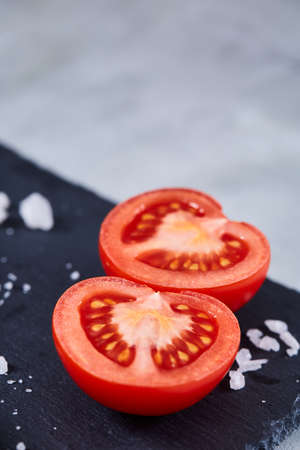 fresh tomatoes with green leaves on black stony board over white textured background, top view, close-up, selective focus. Delicious healthy appetizer. Fresh gourmet ingredient. Spring food background. Dietary product. Healthy food concept.の写真素材