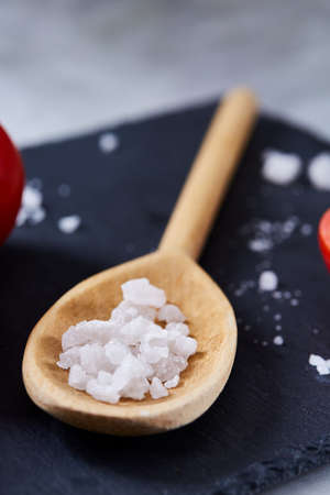 Fresh tomatoes and a spoon of salt on black stony board over white background, close-up, selective focus. Perfect vegetable still life. Delicious healthy appetizer. Fresh gourmet ingredient. Healthy food concept. Spring food background.の写真素材