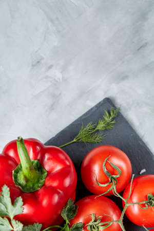 Bunch of fresh tomatoes with green leaves on black stony board over white textured background, top view, close-up, selective focus. Delicious healthy appetizer. Fresh gourmet ingredient. Spring food background. Dietary product. Healthy food concept.の写真素材