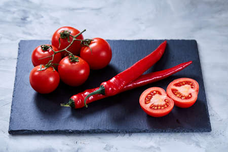 Spring composition of tomato bunch and hot pepper on black flat piece of board over white textured background, top view, close-up. Perfect vegetable still life. Delicious healthy appetizer. Fresh gourmet ingredient. Healthy food concept.の写真素材