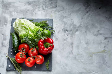 Bunch of fresh tomatoes with green leaves on black stony board over white textured background, top view, close-up, selective focus. Delicious healthy appetizer. Fresh gourmet ingredient. Spring food background. Dietary product. Healthy food concept.の写真素材