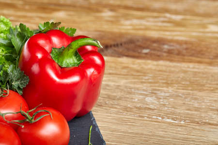 Seasoning close-up still life of assorted fresh vegetables and herbs onwooden rustic background, top view, selective focus. Tomatoes, cucumber, paprica, lettuce, dill and parsley on black stony board. Spring greengrocery. Food background.の写真素材