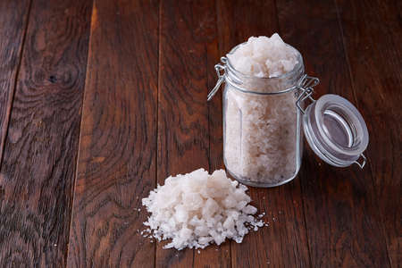 Spa concept. Bath salt pouring out of glass jar on wooden table, close-up, selective focus