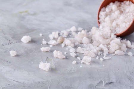 Conceptual composition of sea salt in ceramic bowl and wooden spoon for cooking or spa on white...