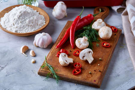 Close-up vegetables for healthy cooking, shallow depth of field, selective focus. Hot pepper, mushrooms, garlic, dill, peppercorns and plate with salt on wooden cutting board. Raw organic veggies on white textured background. Healthy food concept.の写真素材