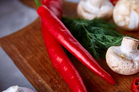 Close-up vegetables for healthy cooking, shallow depth of field, selective focus. Hot pepper, mushrooms, dill and peppercorns on wooden cutting board. Raw organic vegetables on white textured background. Tasty salad ingredients. Healthy food concept.の写真素材