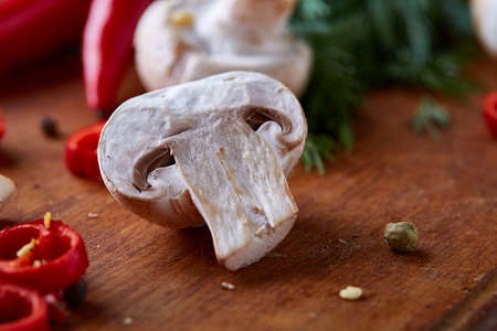 Fresh edible mushrooms togather with hot pepper and herbs on wooden cutting board, close-up, shallow depth of field, selective focus. Organic ingredient for tasty salad. Mediterraniean cuisine. Healthy food concept.の写真素材