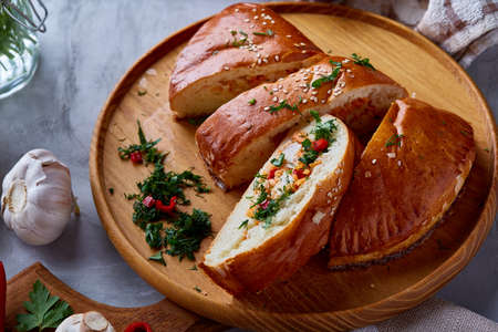 Countryside still life with delicious rustic pastries filled with herbs and vegetables cut on pieces on a wooden plate over a white textured background, selective focus. Yummy puffy meal. Tasty cobbler. Homemade appetizer.の写真素材
