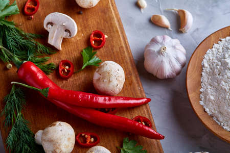 Composition of fresh hot pepper, mushrooms, dill and garlic on cutting board, plate with cooking salt over white textured background, close-up, selective focus. Ingredients ready to make salad. Delicious countryside still life. Food concept.の写真素材