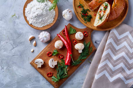 Countryside cuisine still life with tasty homemade pie, fresh mushrooms, hot pepper, garlic and herbs on wooden cutting board over white textured background, selective focus. Studio shot. Delicious rustic appetizer. Food concept.の写真素材
