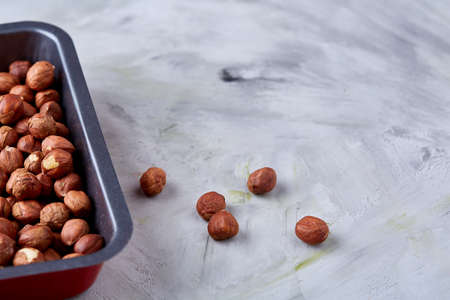 Hazelnut on cooking tray over white textured background, close-up, selective focus, shallow depth of field. Some copy space for your inscription. Nutritious organic snack. Vegetarian protein. Seasonal antioxidant. Healthy food concept.の写真素材