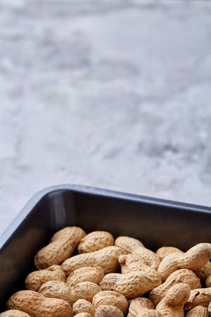 Unpeeled raw peanut on baking tray over white textured background, selective focus, shallow depth of...