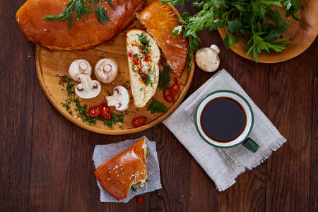 Countryside still life with delicious rustic pastries, cup of coffee, herbs and vegetables on a wooden cutting board over a vintage wooden background, selective focus. Yummy puffy meal. Tasty cobbler. Homemade appetizer.の写真素材