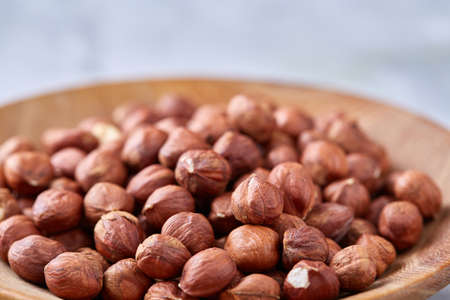 Hazelnuts in wooden plate on white textured background with copy space, top view, close-up, selective focus, shallow depth of field. Nutritious organic snack. Vegetarian protein. Seasonal antioxidant. Healthy food concept.の写真素材