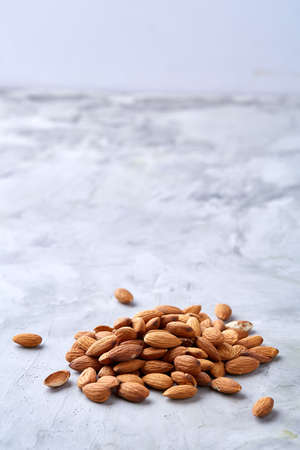 A pile of shelled almond nuts isolated against white textured background, close-up, top view, selective focus. Some copy space from above. Uncooked protein. Natural oil source. Diet ingredient for weight control. Healthy food concept.の写真素材