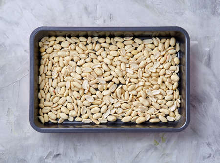 Peeled peanut on baking tray over white textured background, selective focus, shallow depth of field. Ready to bake. Healthful and nutritious snack. Delicious ready to cook nuts. Healthy lifestyle concept.の写真素材