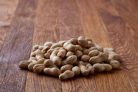 Unpeeled peanuts on a wooden background, top view, selective focus, shallow depth of field. Some copy space for your text. Studio shot. Organic nutritious ingredient. Gourmet appetizer. Tasty roast snack. Healthy food conceptの写真素材