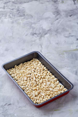 Peeled peanut on baking tray over white textured background, selective focus, shallow depth of field, vertical. Ready to bake. Healthful and nutritious snack. Delicious ready to cook nuts. Healthy lifestyle concept.の写真素材