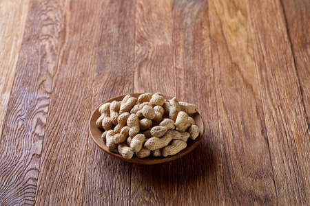 Unpeeled peanuts in wooden bowl over rustic wooden background closeup, selective focus. Some copy space for your text. Healthful and nutritious snack. Delicious ingredient for your every day cooking. Healthy lifestyle concept.の写真素材