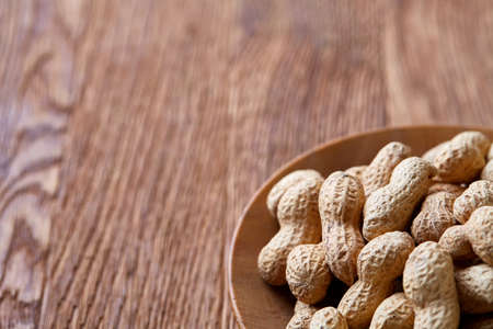 Unpeeled peanuts in wooden bowl over rustic wooden background closeup, selective focus. Some copy space for your text. Healthful and nutritious snack. Delicious ingredient for your every day cooking. Healthy lifestyle concept.の写真素材