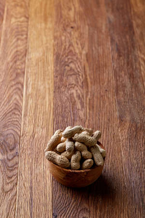 Unpeeled peanuts in wooden bowl over rustic wooden background closeup, selective focus. Some copy space for your text. Healthful and nutritious snack. Delicious ingredient for your every day cooking. Healthy lifestyle concept.の写真素材