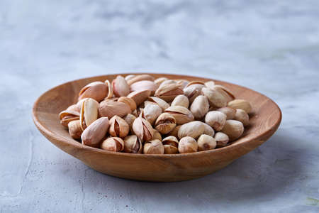 Salted pistachios on a wooden plate over white background, top view, close-up, selective focus. Tasty organic snack. Healthy food for healthy life. Food concept. Natural nutritious nut. Delicious appetizer.の写真素材