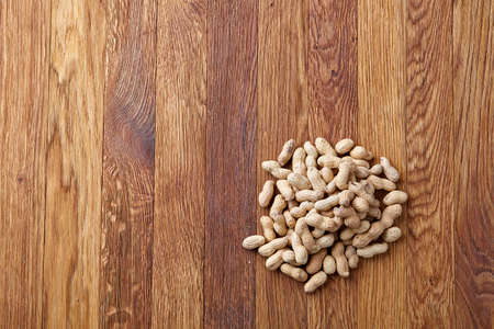 Unpeeled peanuts on a wooden background, top view, selective focus, shallow depth of field. Some copy space for your text. Studio shot. Organic nutritious ingredient. Gourmet appetizer. Tasty roast snack. Healthy food conceptの写真素材