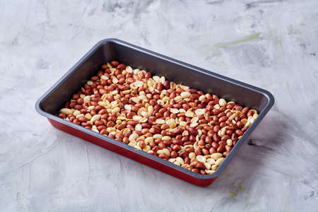 Mix of peeled raw peanut on baking tray over white textured background, selective focus, shallow...