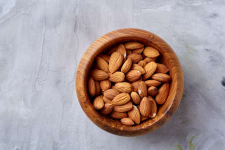 Wooden bowl of almonds on white textured background, top view, close-up, selective focus. Raw natural organic almond nuts. Healthy food for life. Some copy space. Uncooked protein. Natural oil source. Diet ingredient.の写真素材