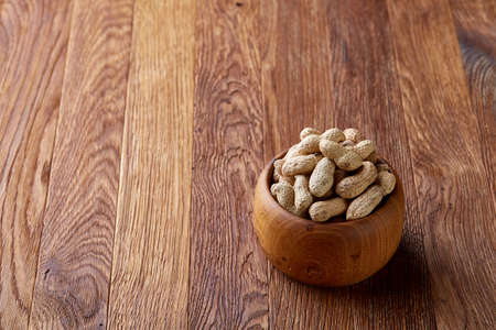 Unpeeled peanuts in wooden bowl over rustic wooden background closeup, selective focus. Some copy space for your text. Healthful and nutritious snack. Delicious ingredient for your every day cooking. Healthy lifestyle concept.の写真素材
