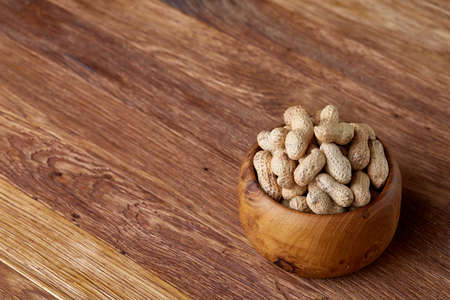 Unpeeled peanuts in wooden bowl over rustic wooden background closeup, selective focus. Some copy space for your text. Healthful and nutritious snack. Delicious ingredient for your every day cooking. Healthy lifestyle concept.の写真素材