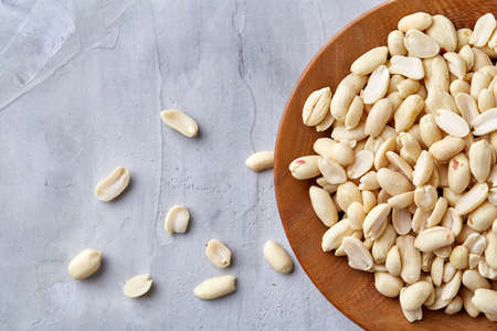 Shelled peanuts in wooden plate isolated over white textured background, top view, close-up. Some copy space. Organic nutritious ingredient. Gourmet appetizer. Tasty roast snack. Healthy food conceptの写真素材