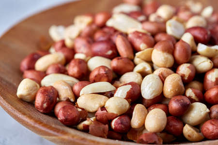 Mix of raw shelled peanuts in wooden plate isolated over white textured background, top view, close-up, shallow depth of field. Some copy space. Organic nutritious ingredient. Gourmet appetizer. Tasty roast snack. Healthy food conceptの写真素材