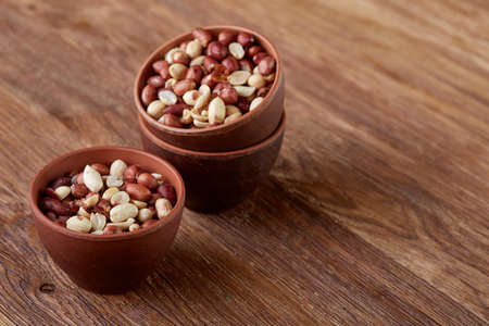 Two ceramic bowls shelled raw peanuts mix isolated over rustic wooden background, top view,...