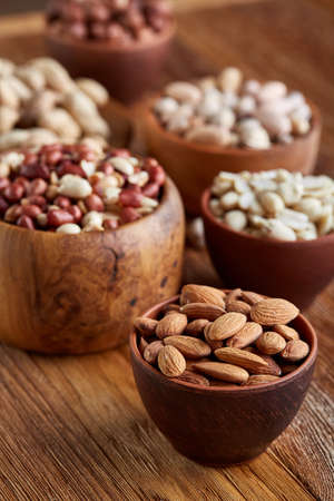 A composition from different varieties of nuts in a wooden bowls over rustic background: hazelnuts,...