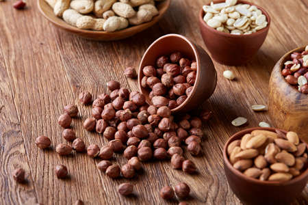 A composition from different varieties of nuts in a wooden bowls over rustic background: hazelnuts, almonds, pistachios. Close-up, selective focus. Delicious nutritious mix. Organic antioxidant. Dieting assortment. Healthy food concept.の写真素材