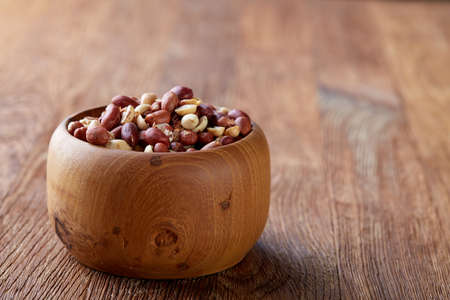 Shelled raw peanuts mix in wooden bowl isolated over rustic wooden background, top view, close-up....