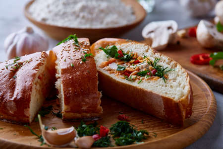 Countryside cuisine still life with tasty homemade pie, fresh mushrooms, hot pepper, garlic and herbs on wooden cutting board over white textured background, selective focus. Studio shot. Delicious rustic appetizer. Food concept.の写真素材
